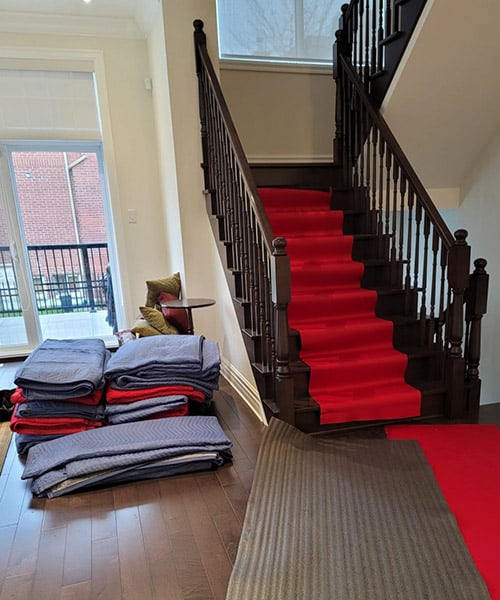 a house with red carpet going up the staircase with a stack of padded furniture covers next to it