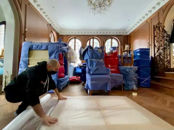 a Crown Movers team member carefully wrapping large items on the floor with furniture already wrapped behind him